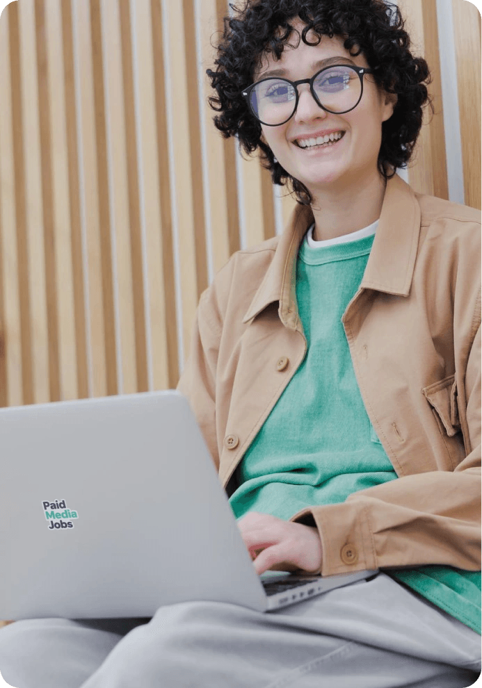 Smiling woman working on a laptop with a Paid Media Jobs sticker