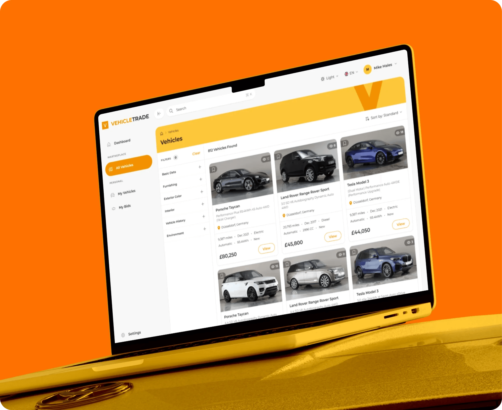 Vehicle trading web app listing cars with photos and prices, on a laptop.